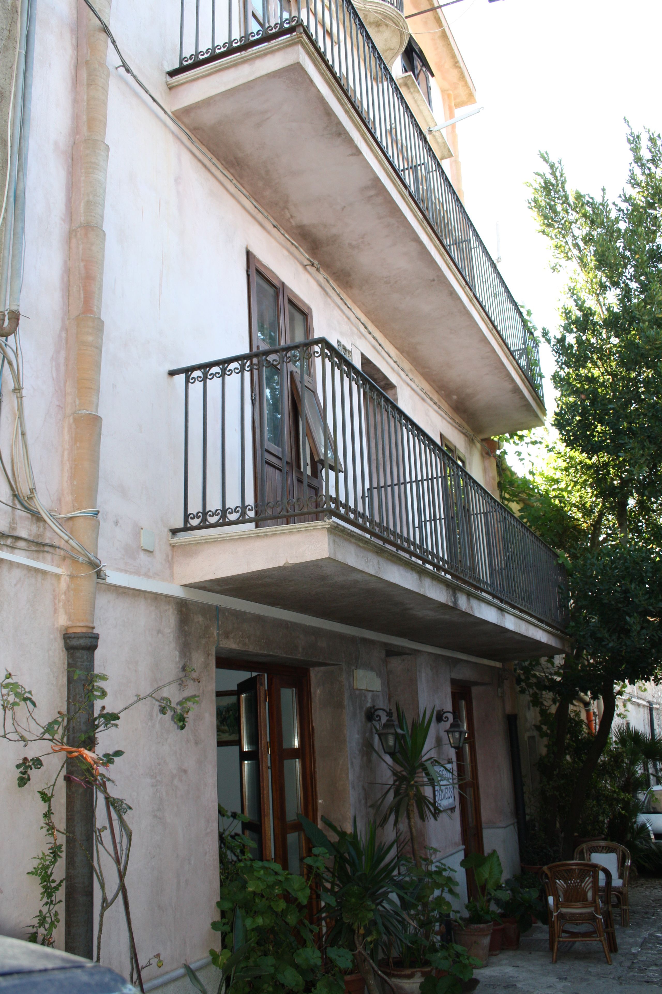 A two-story building with balconies, potted plants, and outdoor furniture.