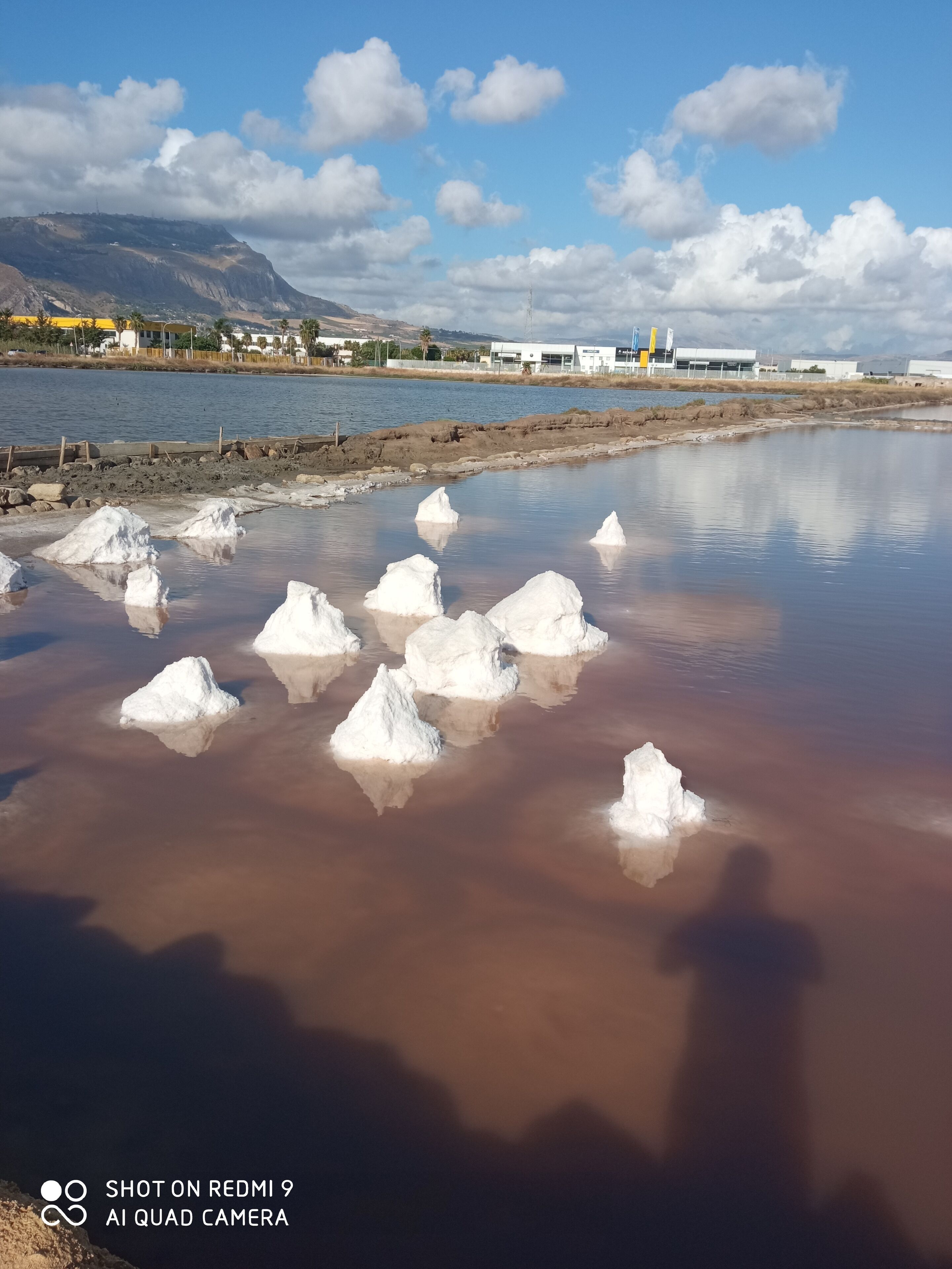 Un cuerpo de agua con formaciones de hielo blanco, cielo despejado y edificios a lo lejos.