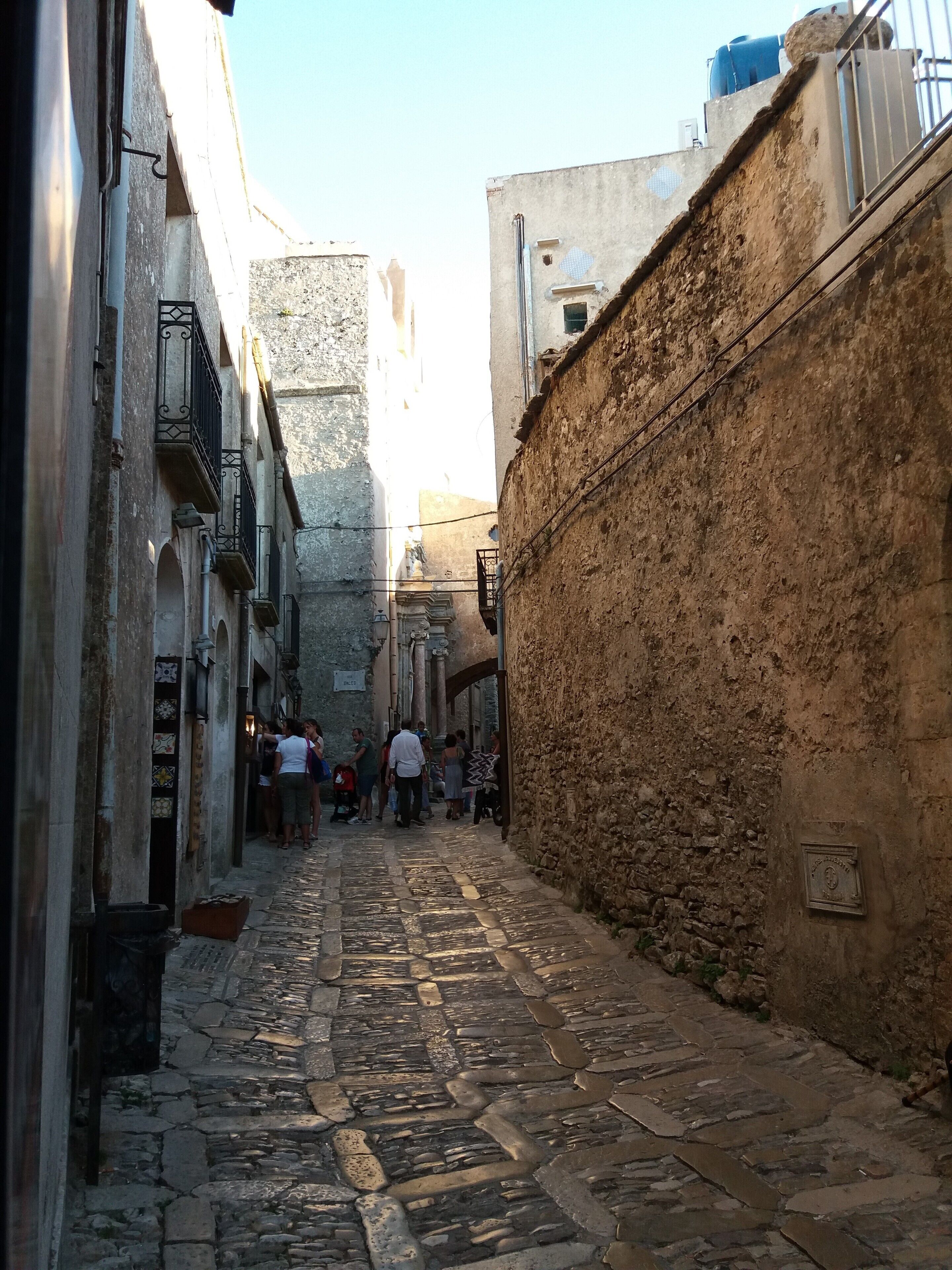 Uma rua de paralelepípedos estreita, ladeada por edifícios antigos com paredes de pedra e grades de metal.