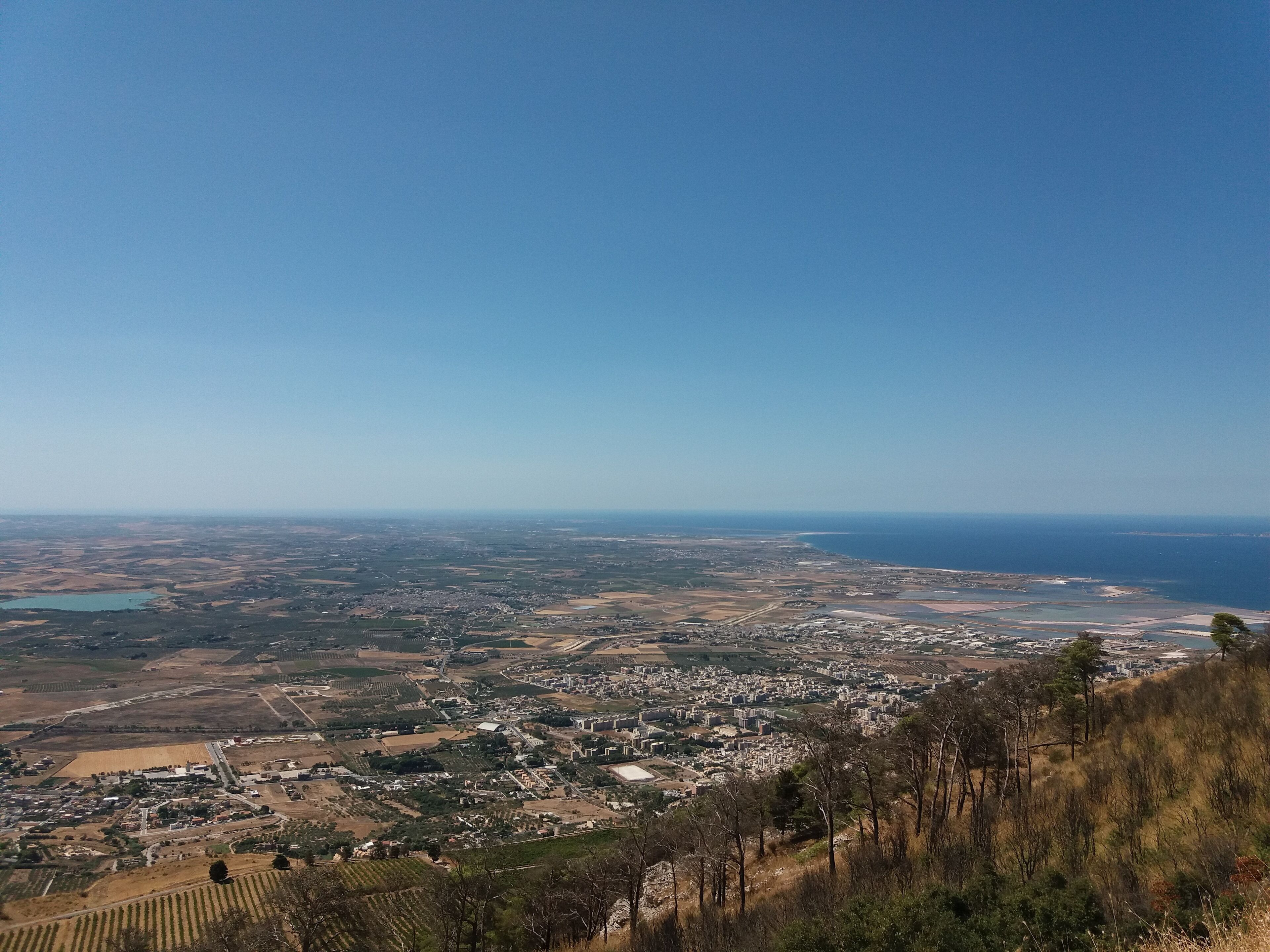 Une vue panoramique d’une ville côtière, avec un mélange de zones urbaines et agricoles, comprenant des champs, des bâtiments et une côte.