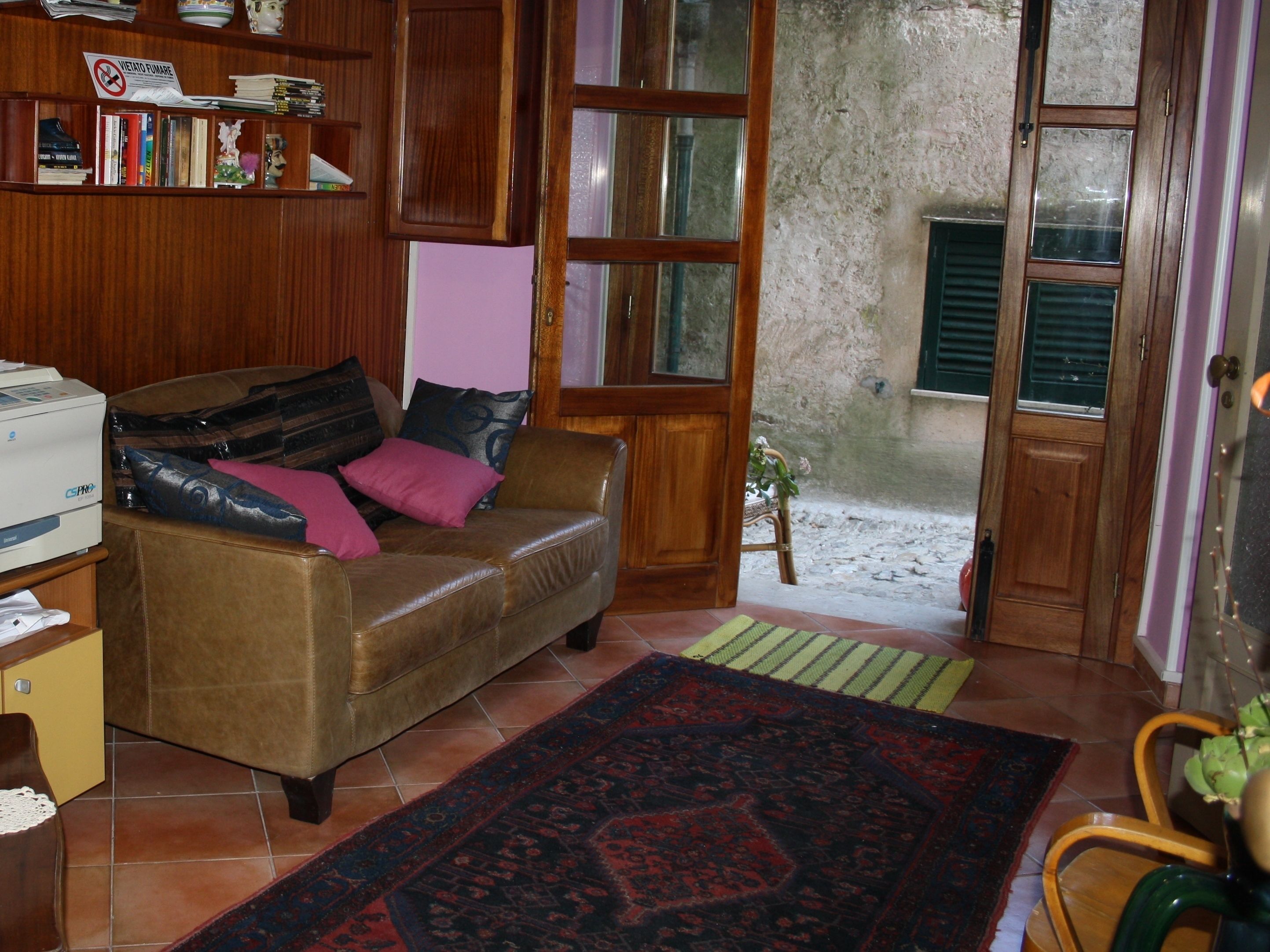Una sala acogedora con un sofá de cuero marrón, una estantería de madera, una impresora y una alfombra estampada.