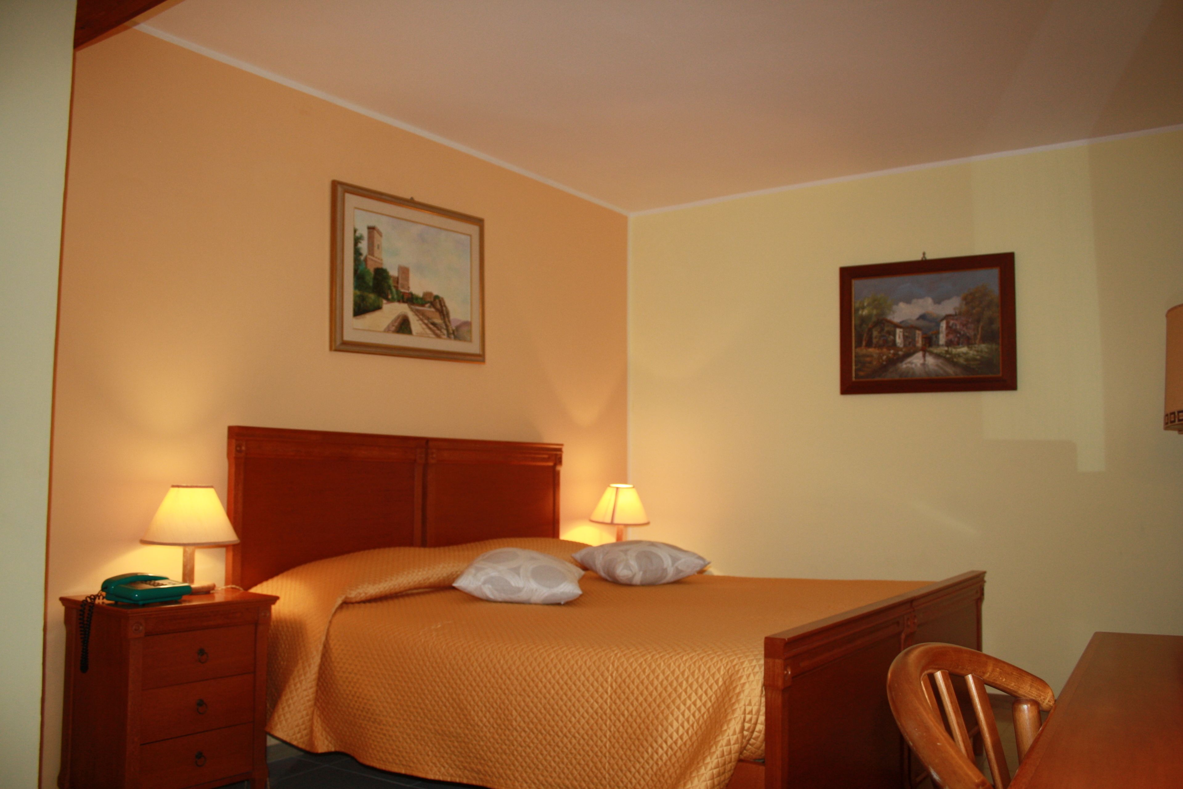 Une chambre d’hôtel comprenant un lit, deux lampes de chevet, une table de chevet en bois, une chaise en bois et deux tableaux encadrés accrochés aux murs.