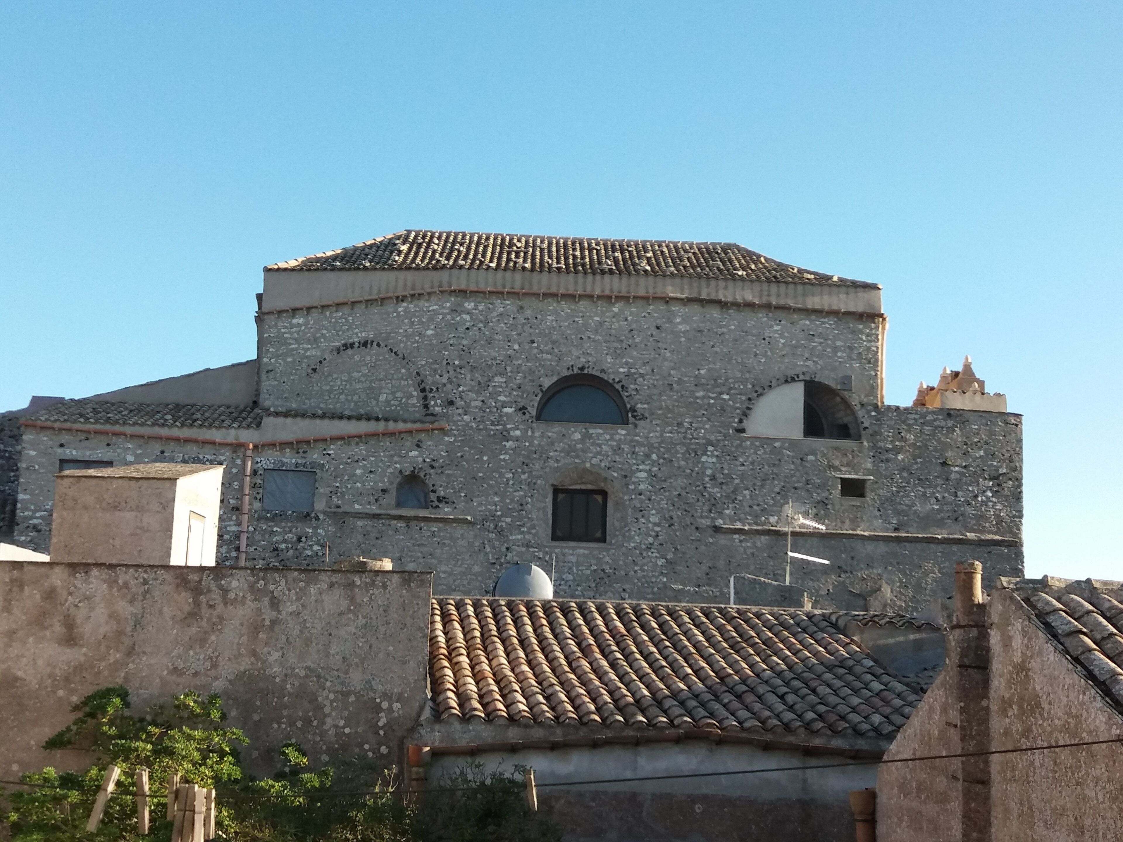 A historic stone building with a tiled roof, arched windows, and a small bell tower.