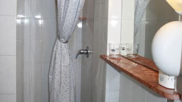 Un baño con cortina de ducha, lavamanos, espejo y estante con artículos de aseo.