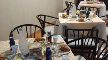 A dining area with tables set for breakfast, including croissants, beverages, and plates.