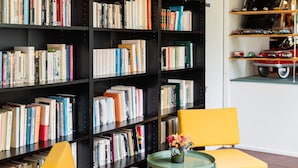 A room with a large bookshelf filled with books, a yellow armchair, a small round table with a vase, and a sign that reads "METEOR D'ALSACE". - Hôtel Les Hauts de Meursault (Meursault)
