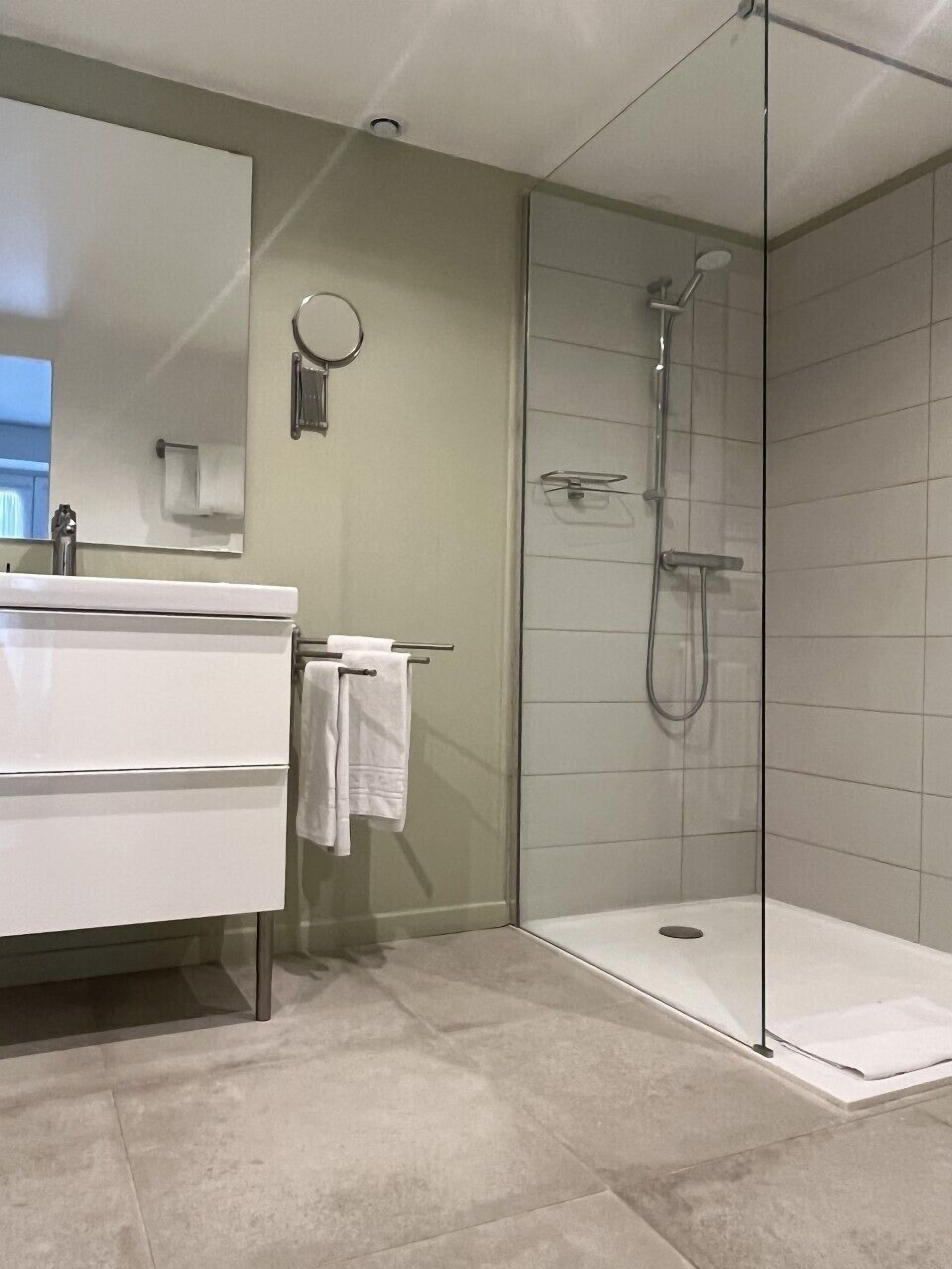 A modern bathroom with a glass-enclosed shower, a white sink, and a mirror.