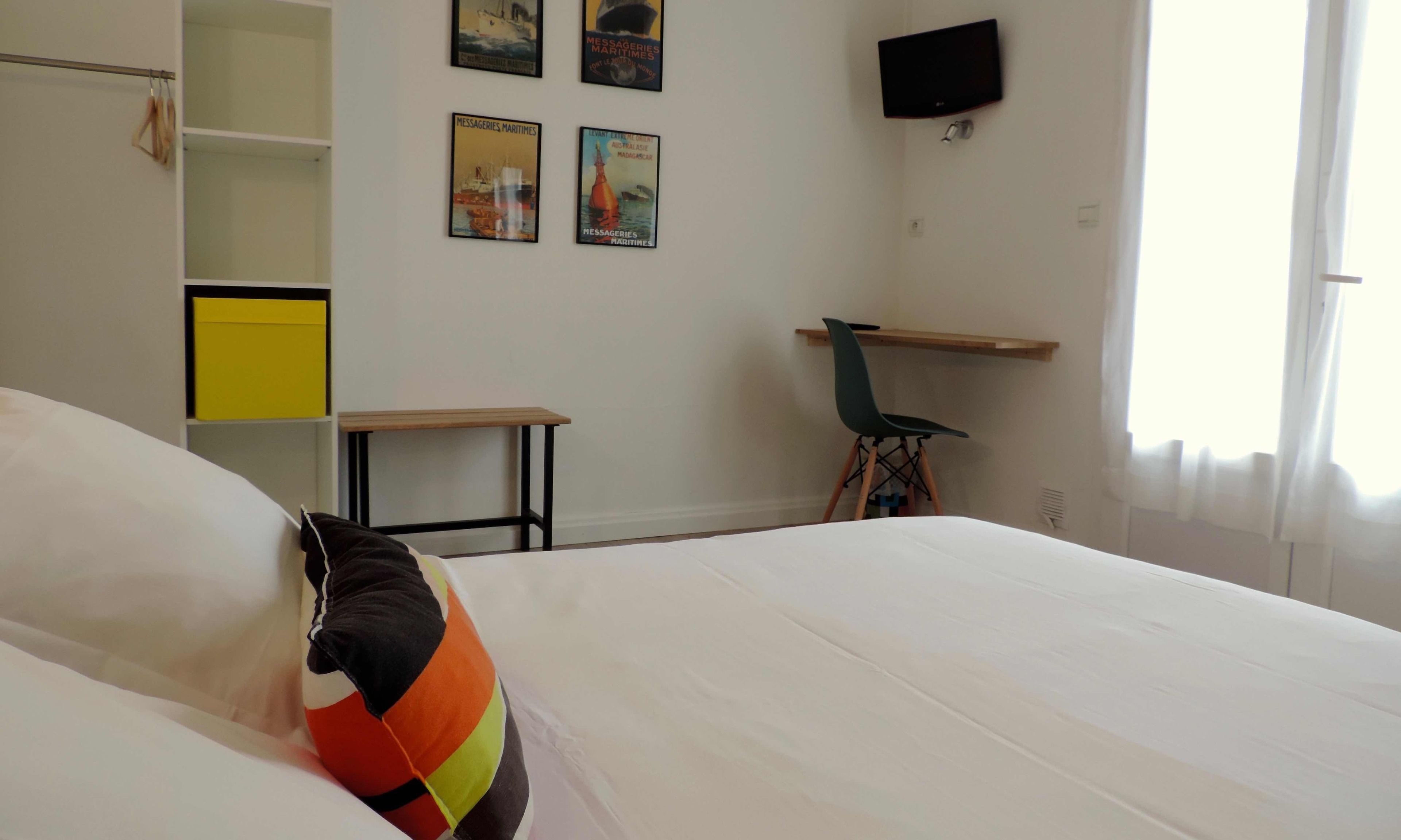 Un dormitorio con cama, escritorio, silla y televisor en la pared.