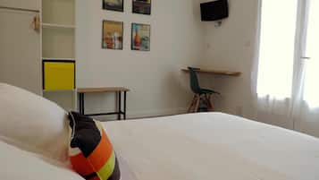 A bedroom with a bed, a desk, a chair, and a TV on the wall.