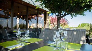 An outdoor dining area with tables set for two, each with a green placemat and wine glasses.