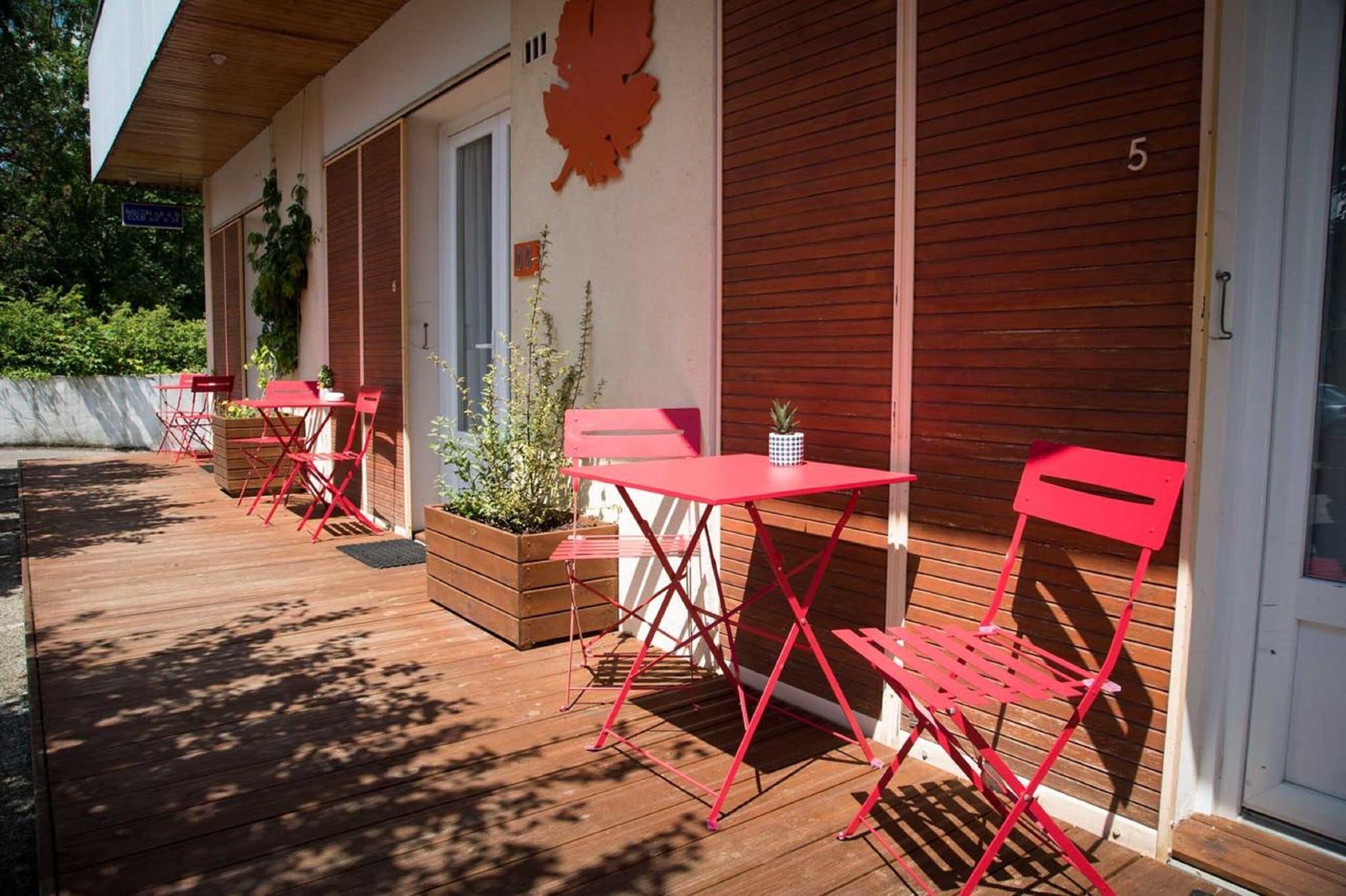 Patio esterno con sedie rosse pieghevoli e un tavolo, un pavimento in legno e un edificio con il numero 5 sulla porta.