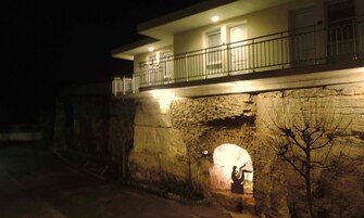 A building with a stone facade, a balcony with a railing, and a lit interior visible through an archway.