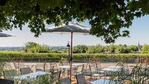 An outdoor patio with tables and chairs, surrounded by greenery and a view of the countryside. - Hôtel Les Hauts de Meursault (Meursault)