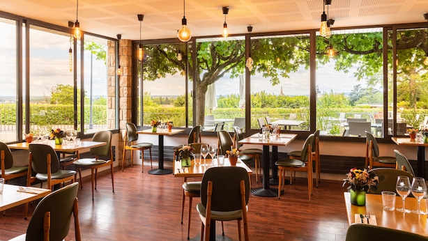 A restaurant with large windows, wooden tables, and chairs. - Hôtel Les Hauts de Meursault (Meursault)