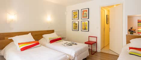 Habitación de hotel con dos camas individuales, una mesita y una puerta que da a otra habitación.