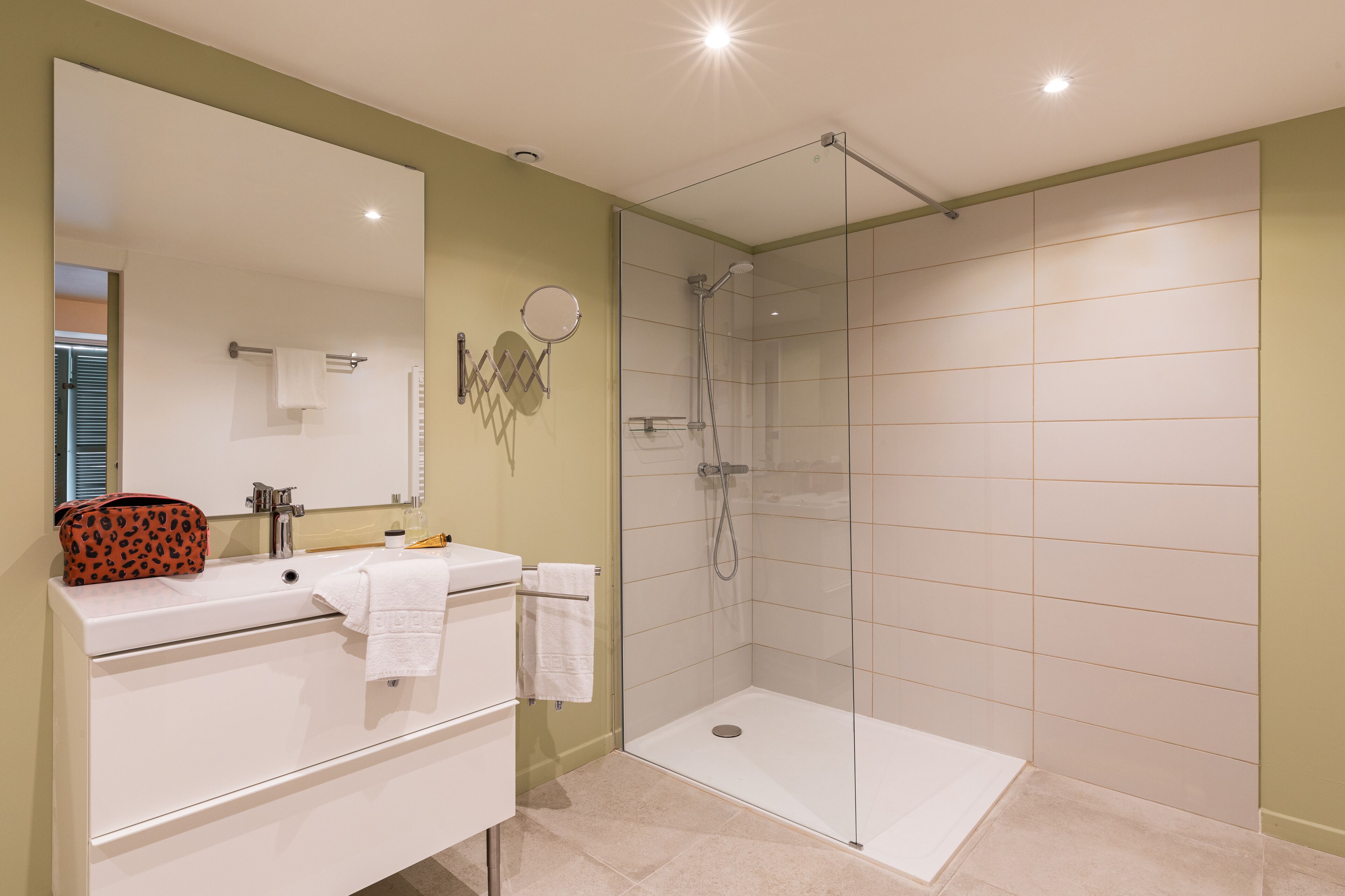 A modern bathroom with a glass shower enclosure, a white sink, and a vanity with a mirror.