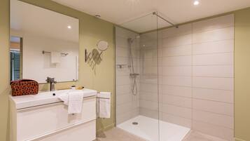 A modern bathroom with a glass shower enclosure, a white sink, and a vanity with a mirror.
