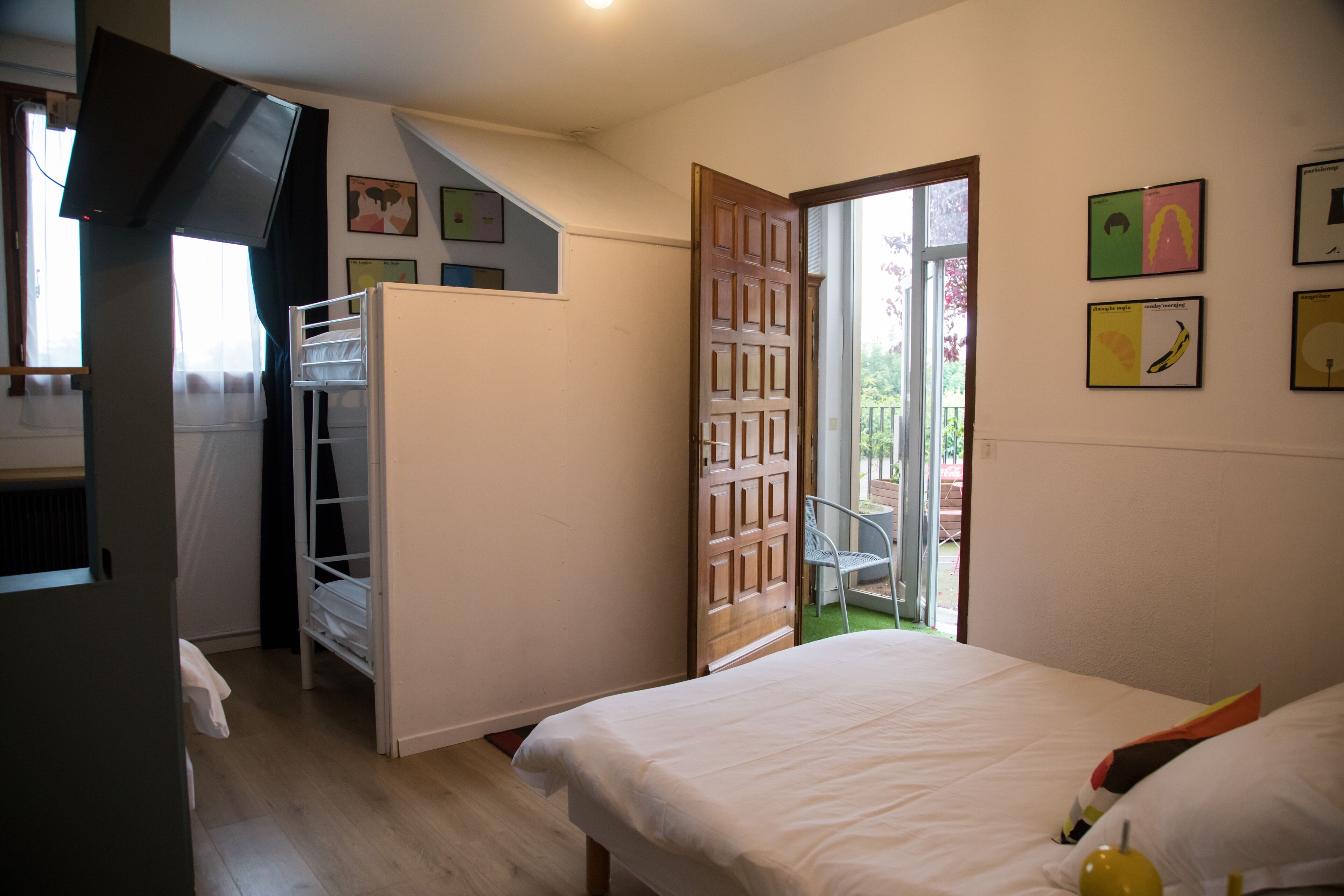 A bedroom with a bed, a wardrobe, a small table, and a chair. There is a door leading to an outdoor area.
