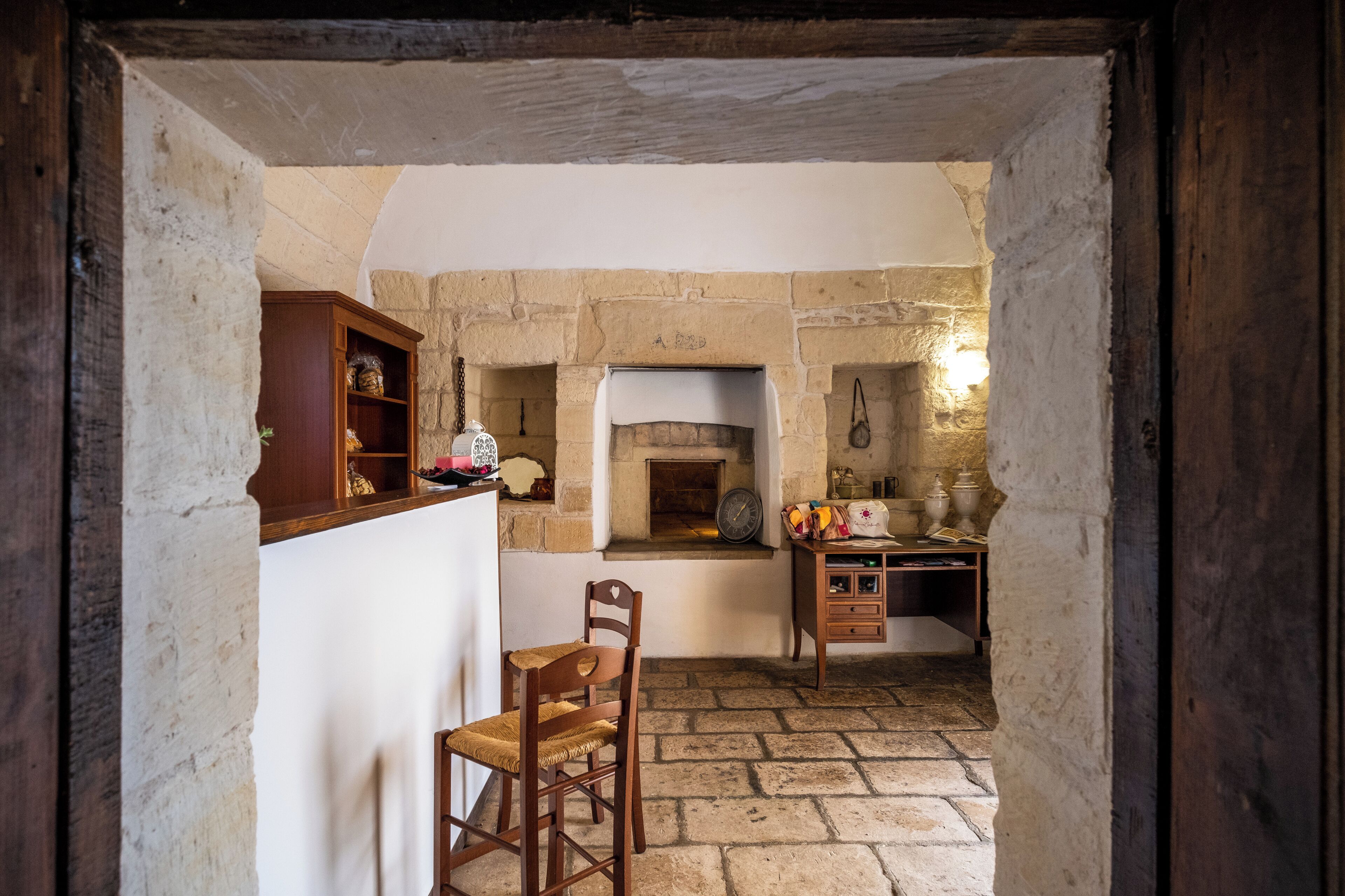 A rustic kitchen with stone walls, a wooden chair, and a wooden cabinet.