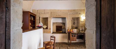 A rustic kitchen with stone walls, a wooden chair, and a wooden cabinet.