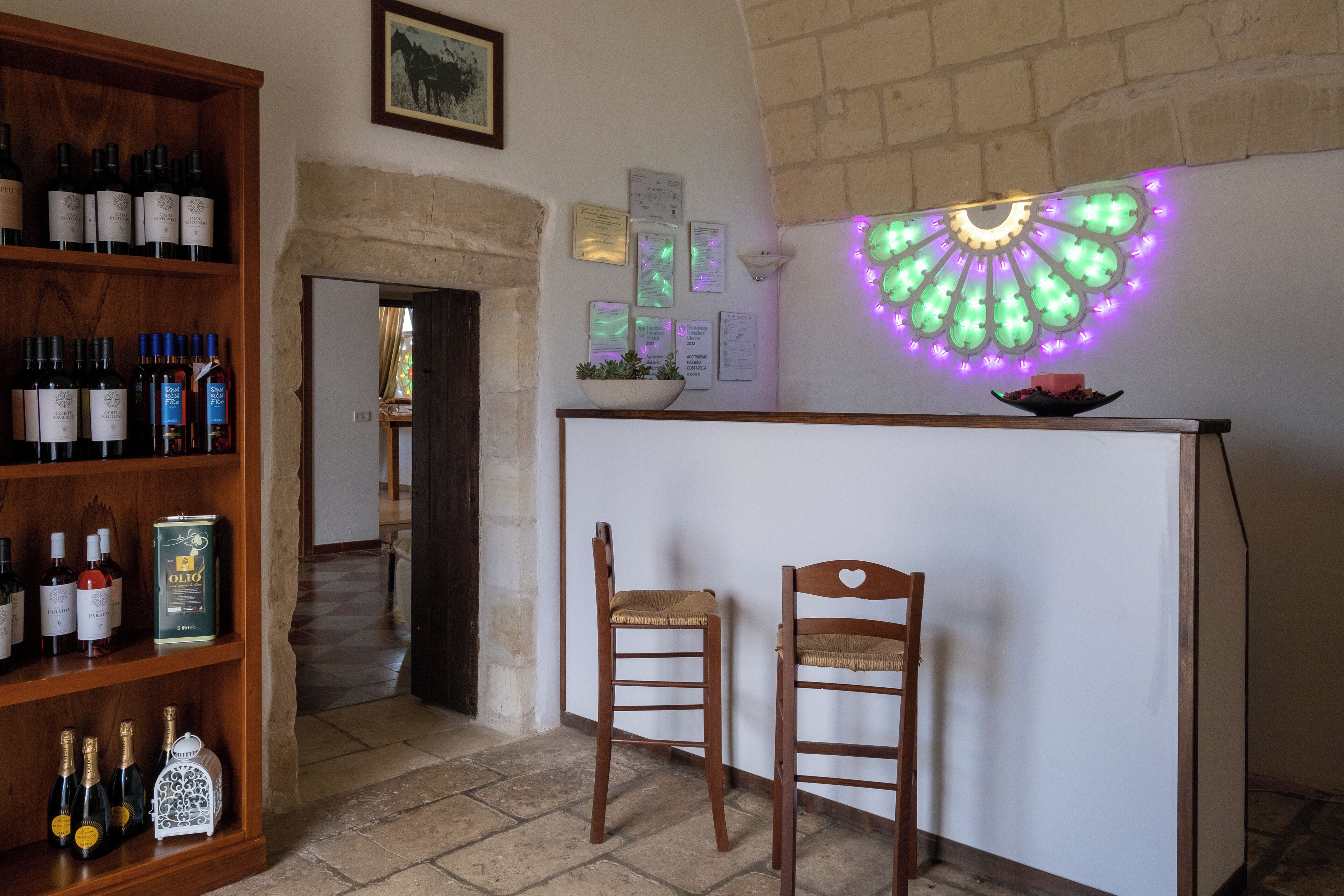 A bar area with wooden shelves of wine bottles, two wooden chairs, and a decorative light fixture.