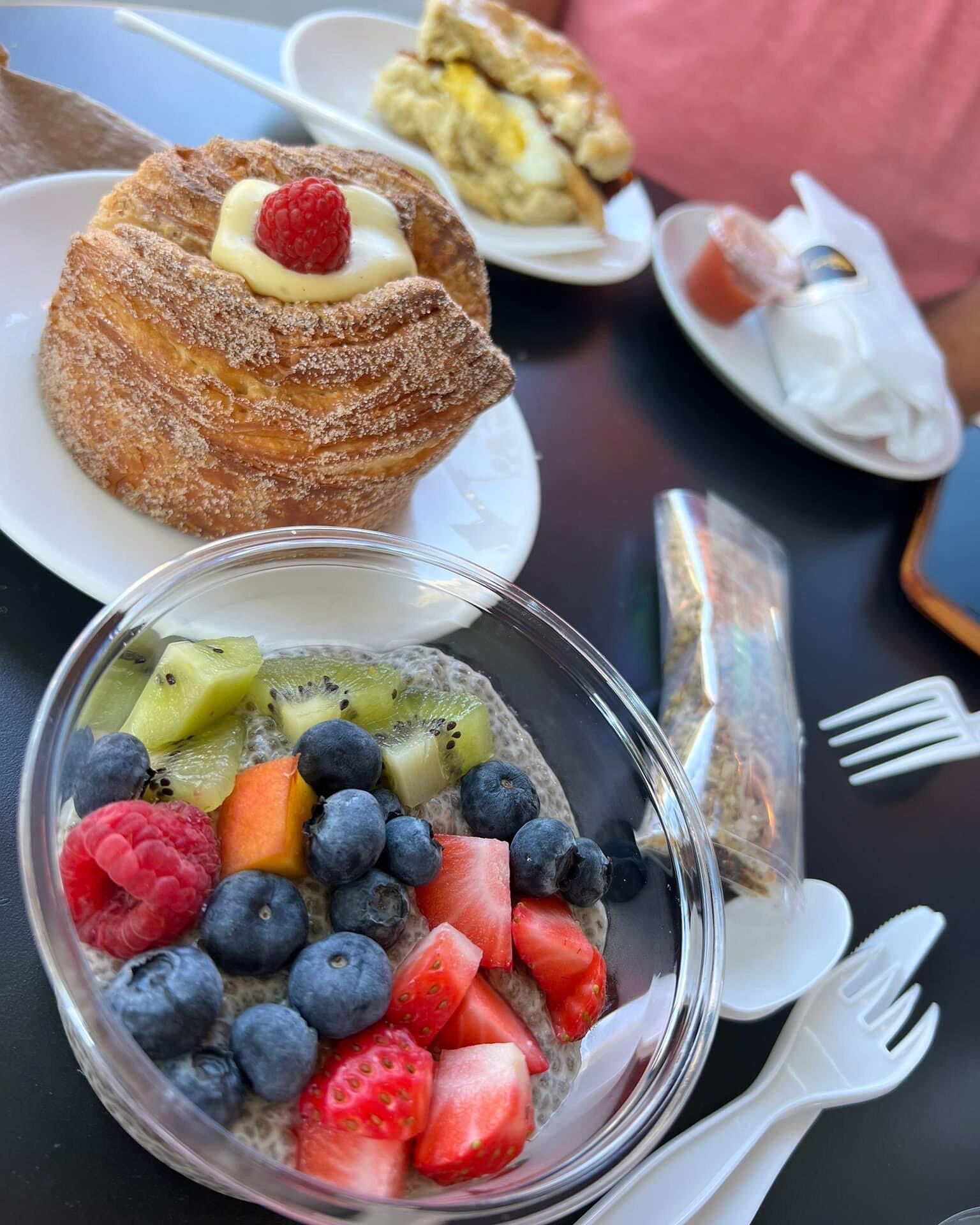 A dessert table with a pastry topped with a raspberry and cream, a bowl of fruit parfait, and a plate of pastries.