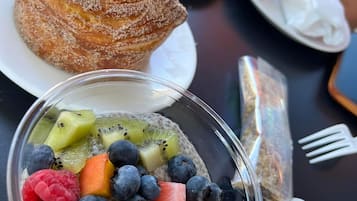 A dessert table with a pastry topped with a raspberry and cream, a bowl of fruit parfait, and a plate of pastries.