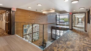A modern hotel lobby with a wooden slatted wall, glass railings, and a patterned carpet. - The Gibson Hotel Great Falls, an Ascend Collection Hotel (Great Falls)