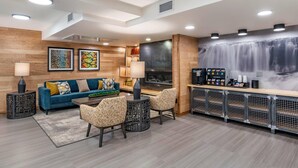 A modern living area with a blue sofa, patterned chairs, a fireplace, and a bar area with a coffee machine. - The Gibson Hotel Great Falls, an Ascend Collection Hotel (Great Falls)