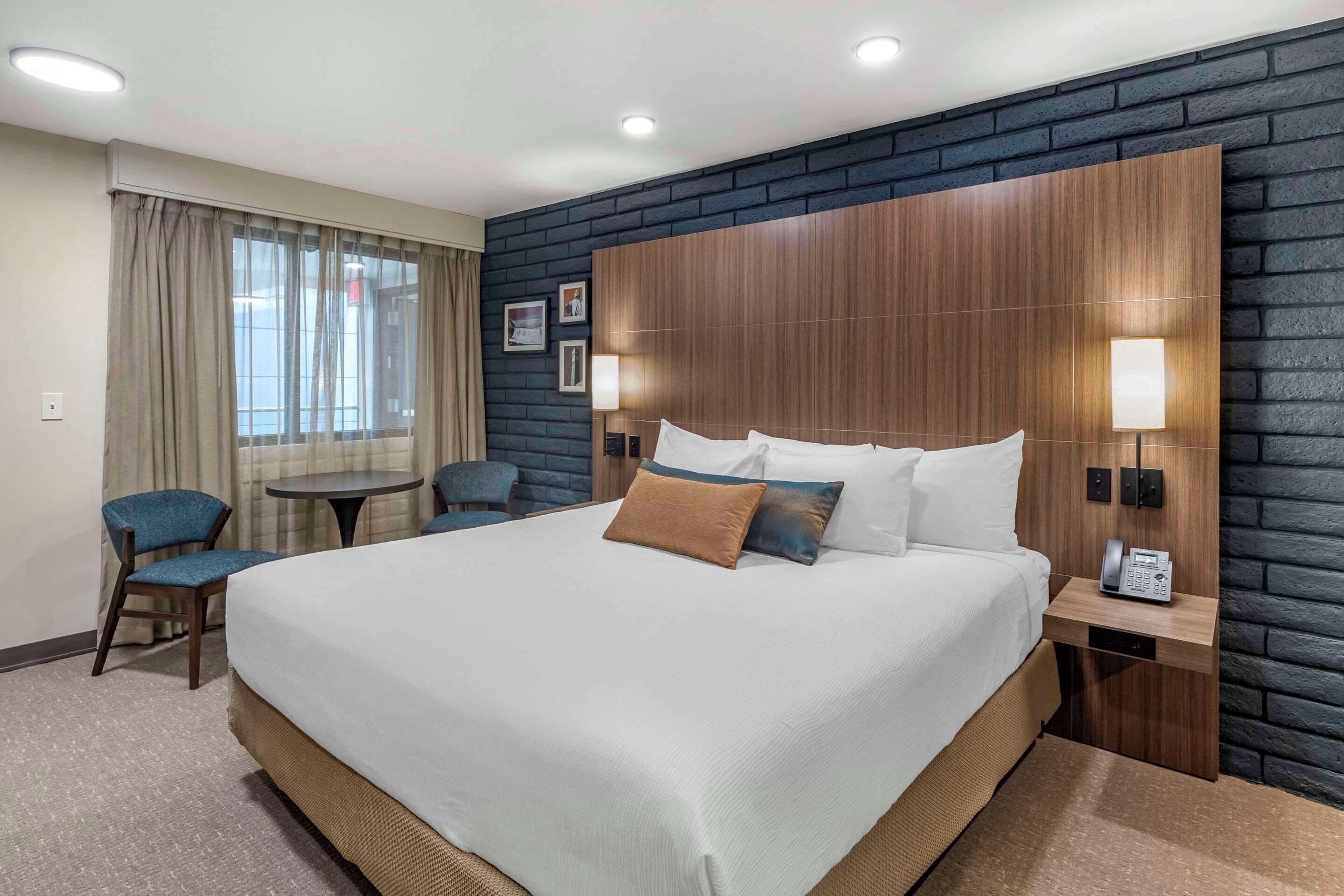A hotel room with a large bed, two bedside tables, a desk, a chair, and a window with curtains.