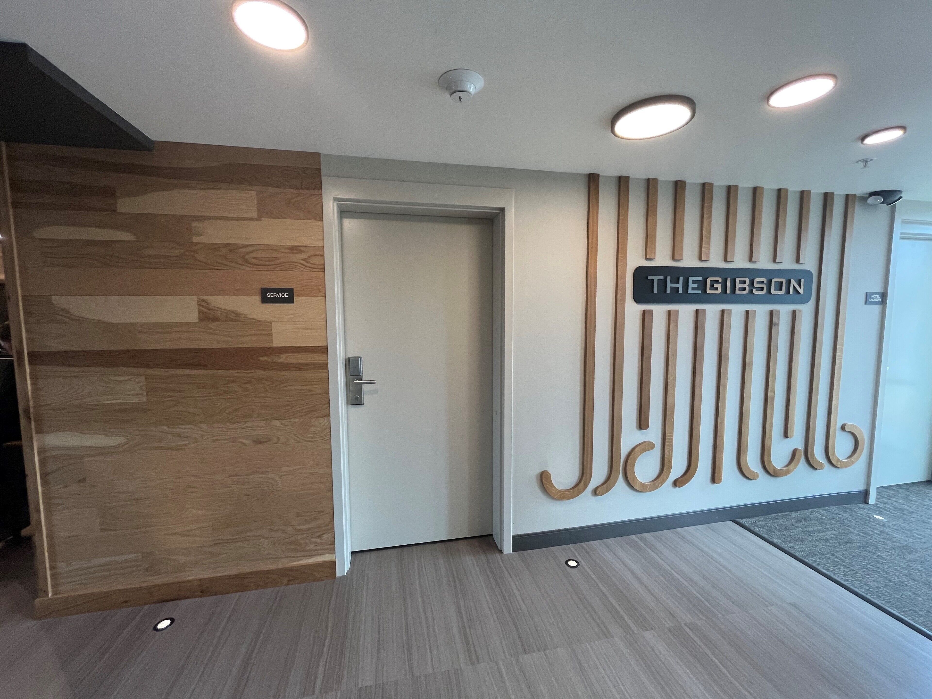 A modern reception area with a wooden panel wall, a service sign, and a nameplate for 'THE GIBSON'.