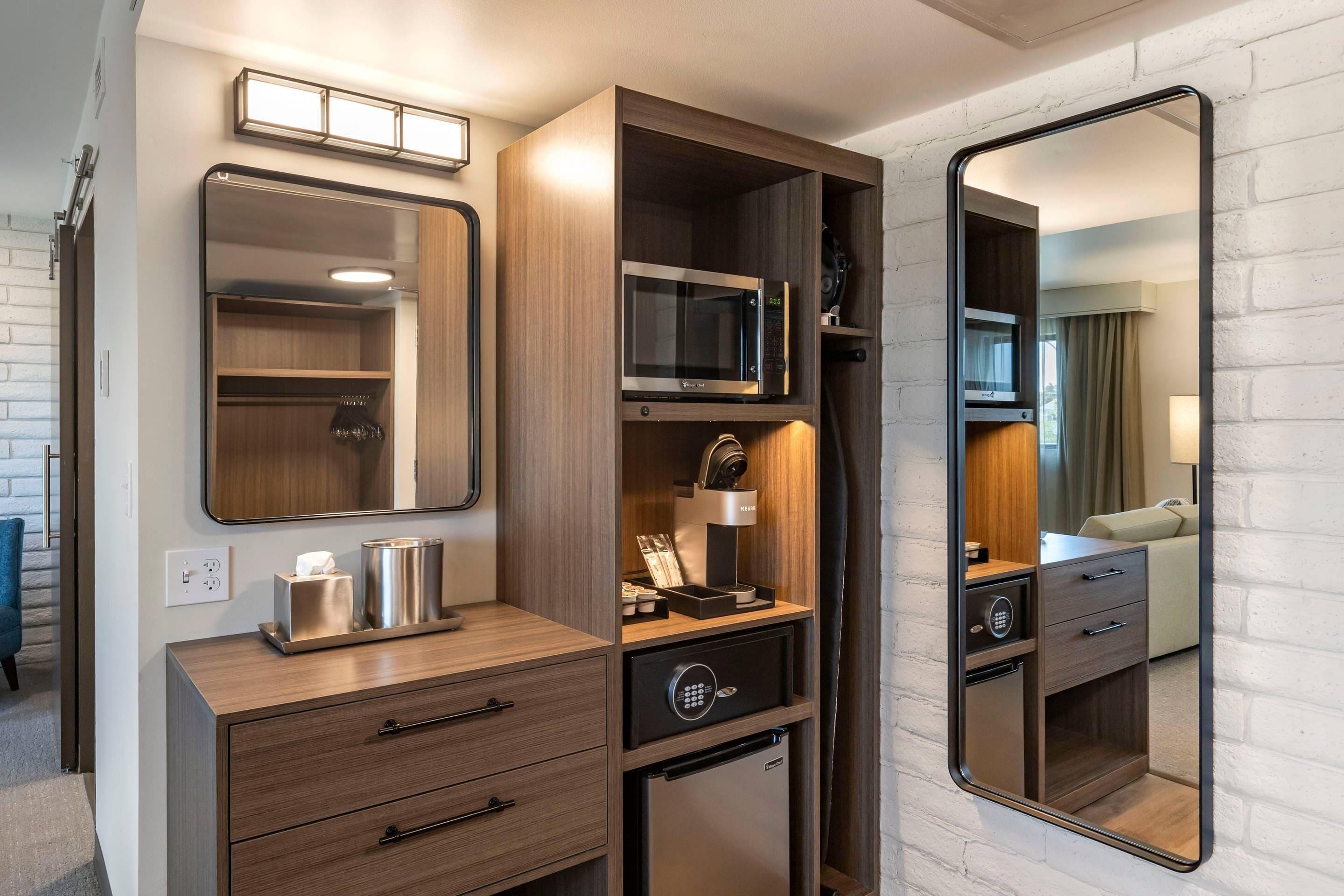 A compact kitchenette with a microwave, refrigerator, and a small cabinet with a mirror.