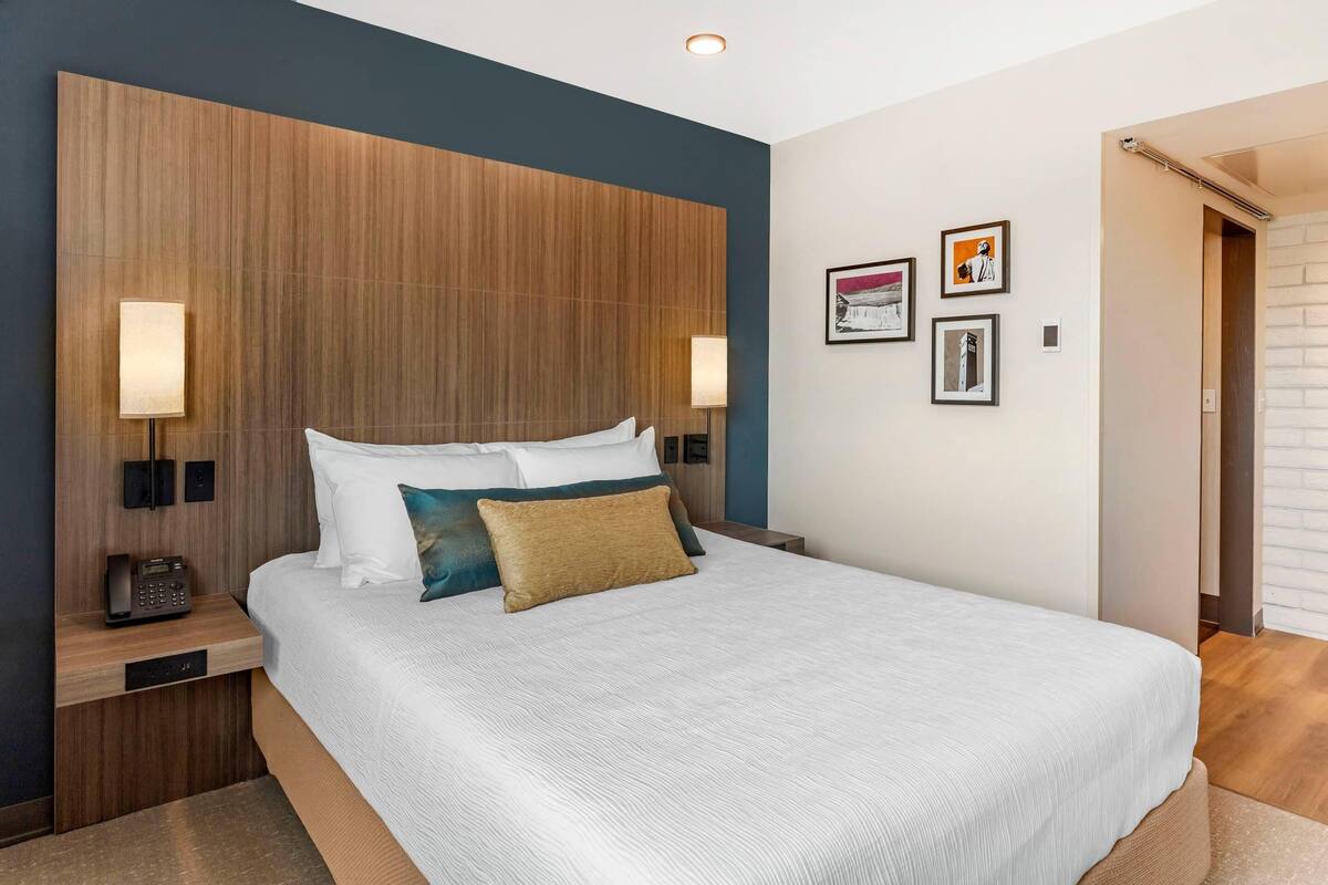 A hotel room with a large bed, bedside lamps, a phone on the nightstand, and framed pictures on the wall.