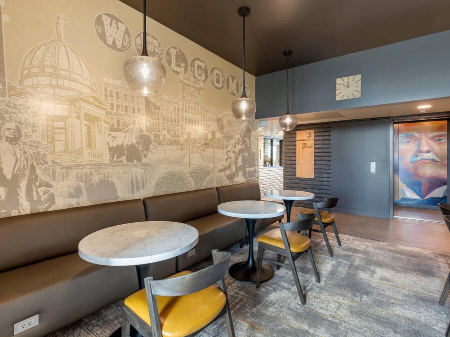 Un interior moderno con un mural que dice 'WELCOME', mesas redondas y asientos acolchados.