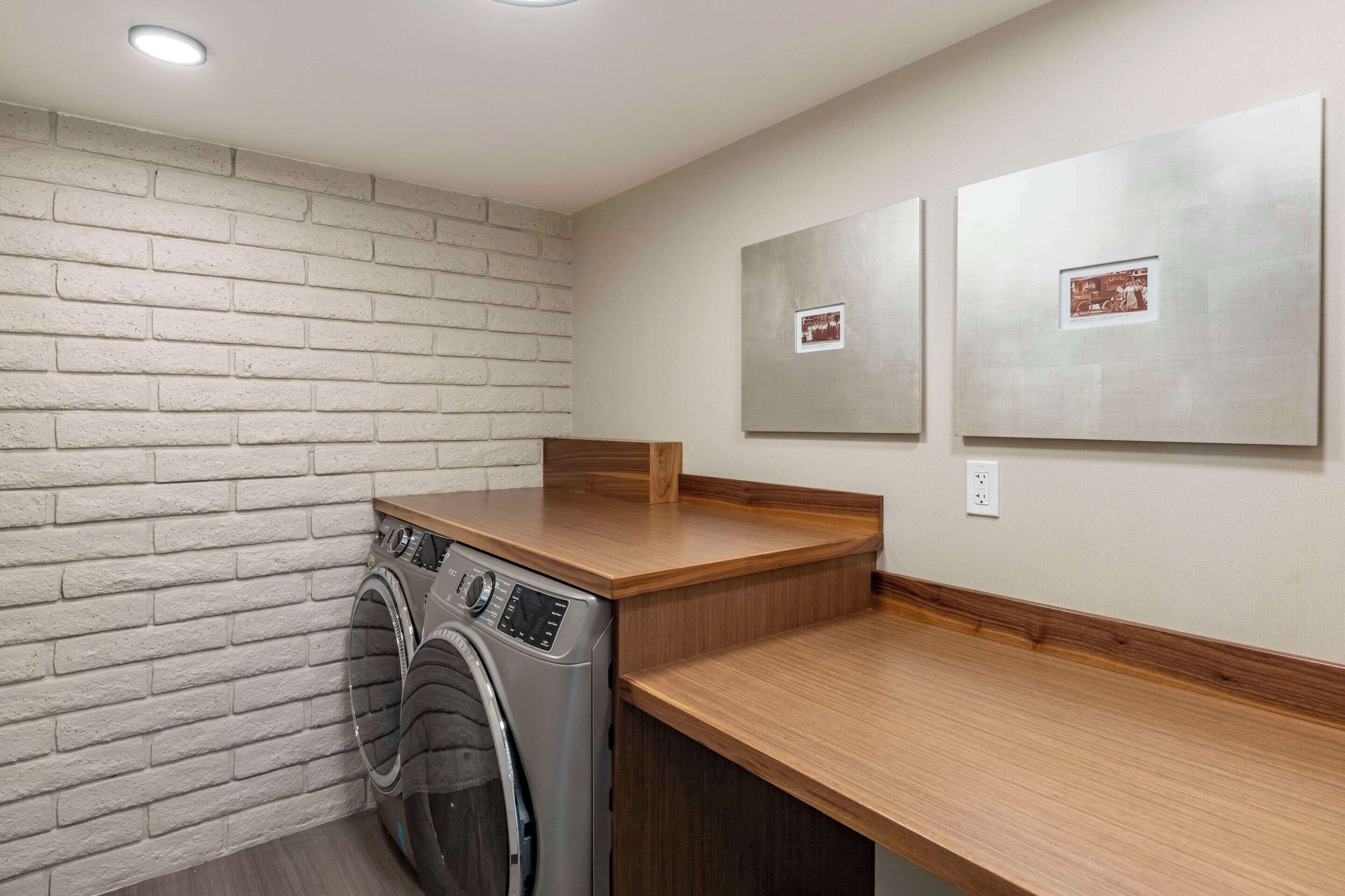 A laundry room with a washing machine, wooden counter, and two framed pictures on the wall.