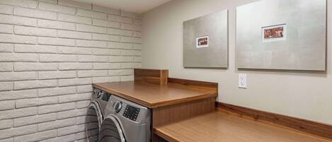 A laundry room with a washing machine, wooden counter, and two framed pictures on the wall.