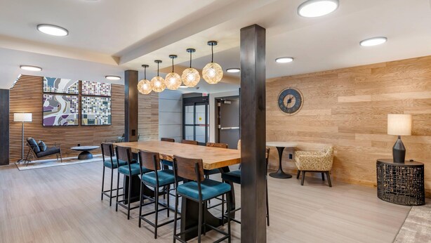 A modern hotel lobby with a wooden reception desk, blue cushioned chairs, and a large wall-mounted clock. - The Gibson Hotel Great Falls, an Ascend Collection Hotel (Great Falls)