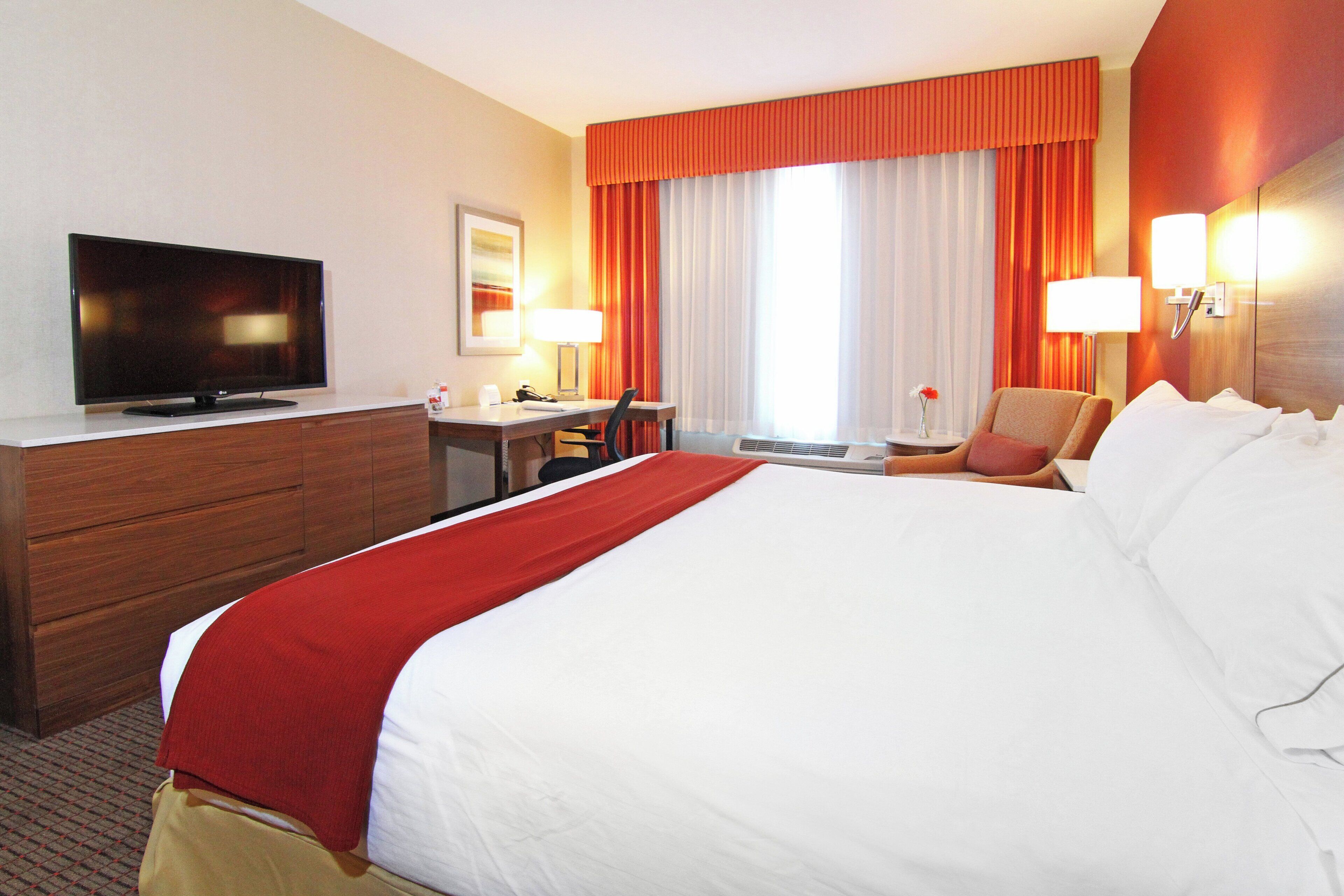 A hotel room with a bed, a desk, a television, and a window with curtains.