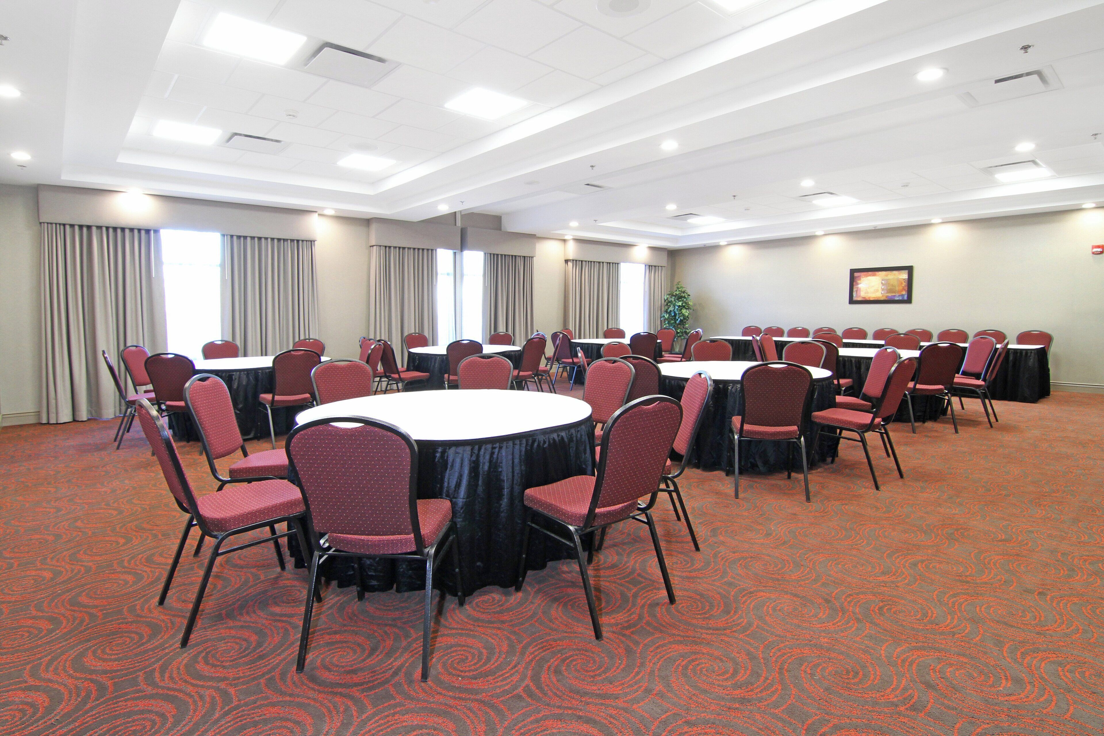 A conference room with round tables and chairs, large windows with curtains, and a patterned carpet.