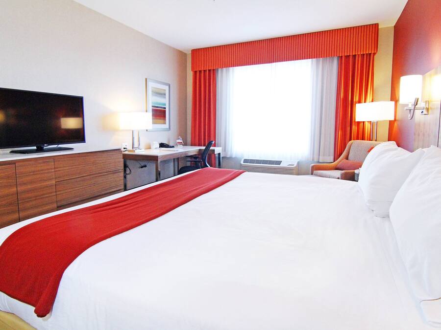 Habitación de hotel con una cama grande, un escritorio con una silla, un televisor y una ventana con cortinas.