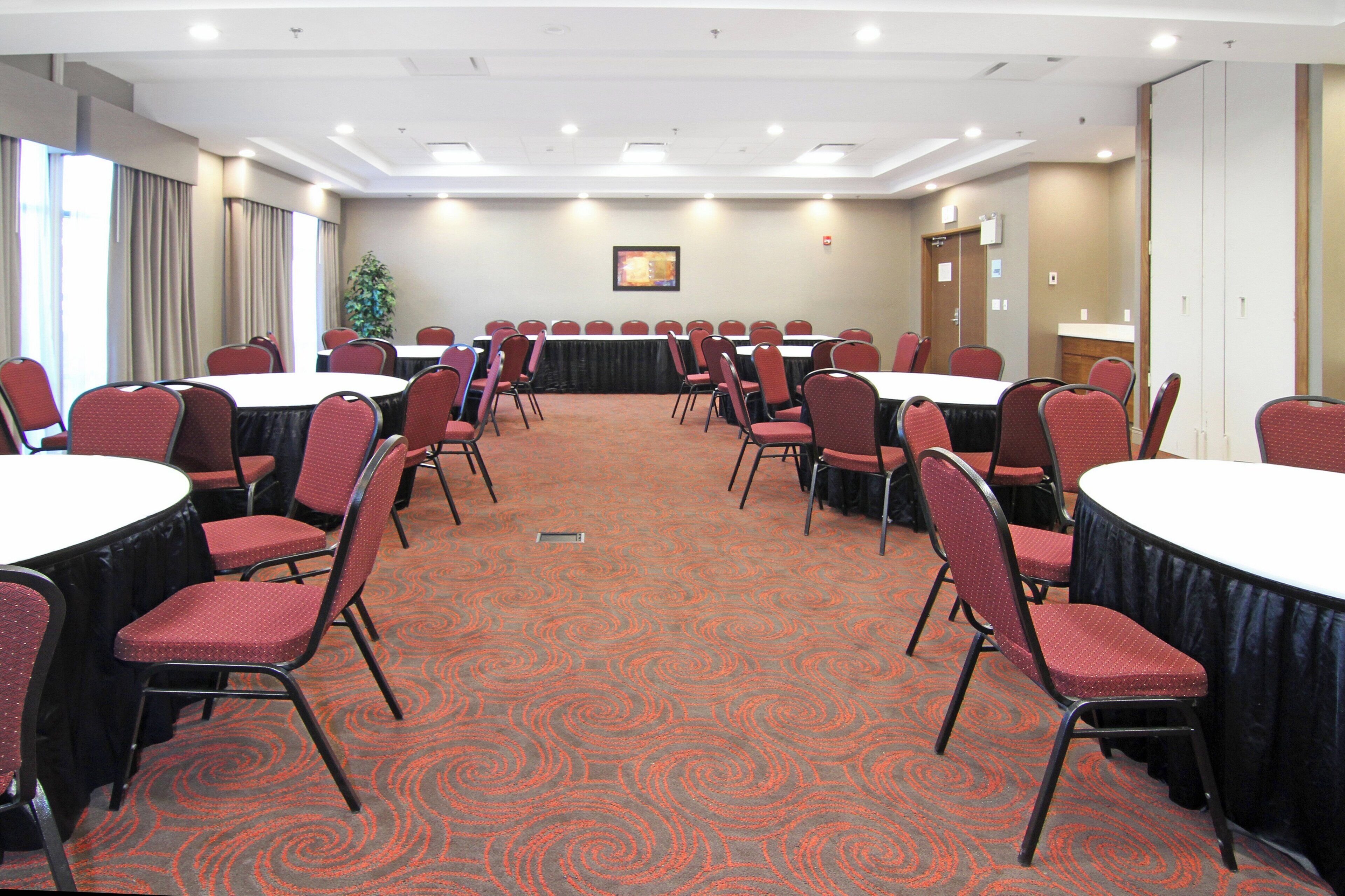 Un salón de conferencias con mesas redondas y sillas, suelo alfombrado y una puerta al fondo.