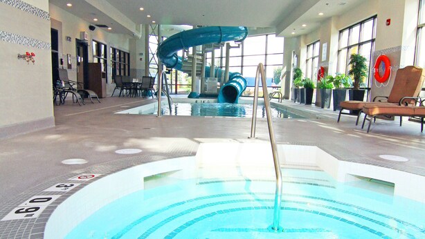 An indoor swimming pool with a blue slide, lounge chairs, and potted plants. - Holiday Inn Express & Suites Calgary NW - University Area by IHG (Calgary)