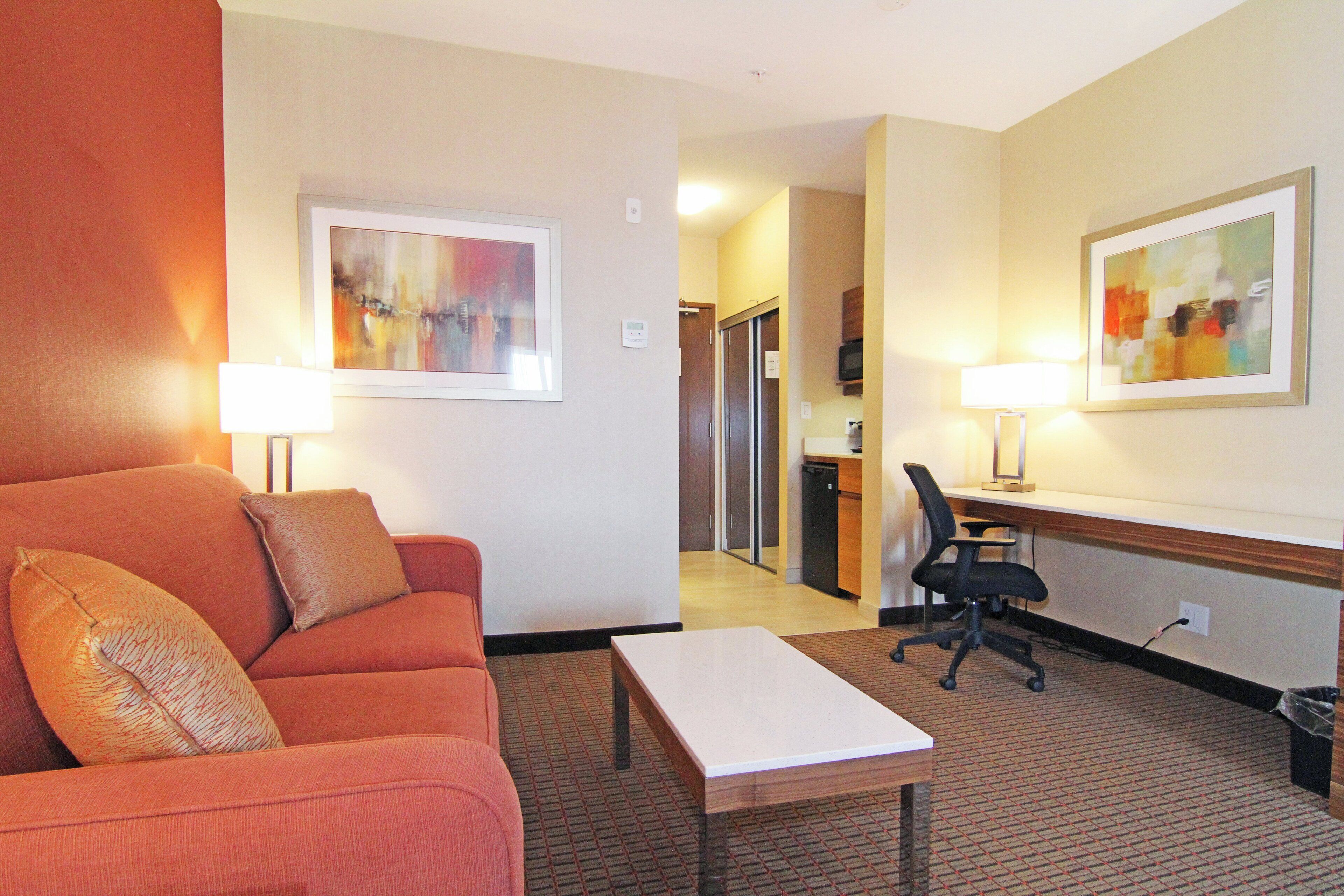 Une chambre d’hôtel avec un canapé, une petite table, un bureau avec une chaise et des œuvres d’art accrochées aux murs.
