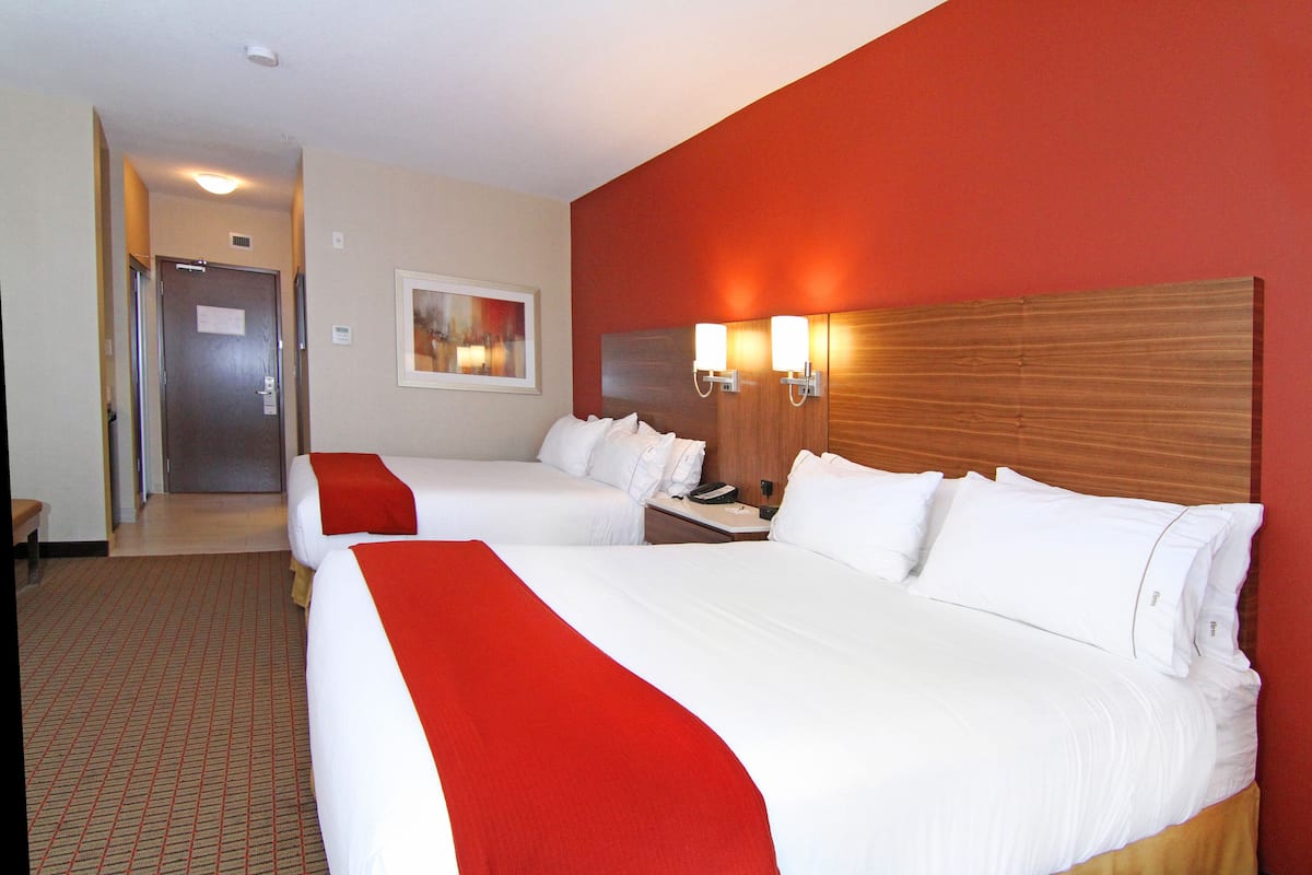 A hotel room with two beds, a wooden headboard, a nightstand, and a painting on the wall.