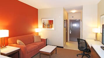 A hotel room with a red wall, a sofa, a small table, a desk with a computer, and a chair.