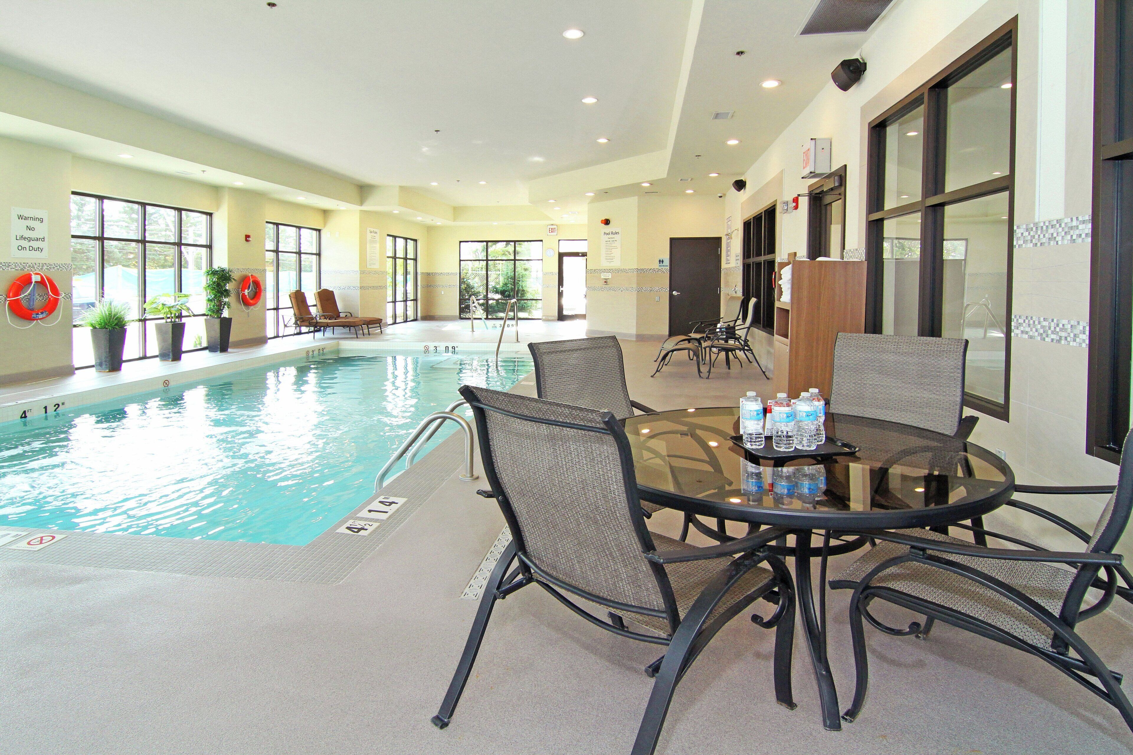Una piscina interior con sillones y mesas, boyas salvavidas y una vista despejada al exterior.