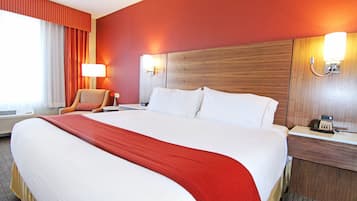 Habitació d'hotel amb un llit gran, una cadira, una tauleta de nit amb una làmpada i un telèfon fixat a la paret.