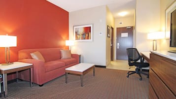 Une chambre d’hôtel avec un mur rouge, un canapé, une table basse, un bureau, une chaise et un lit.