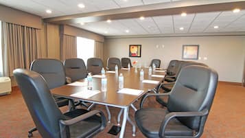 Un salón de conferencias con una mesa larga, varias sillas, botellas de agua y dos cuadros en la pared.
