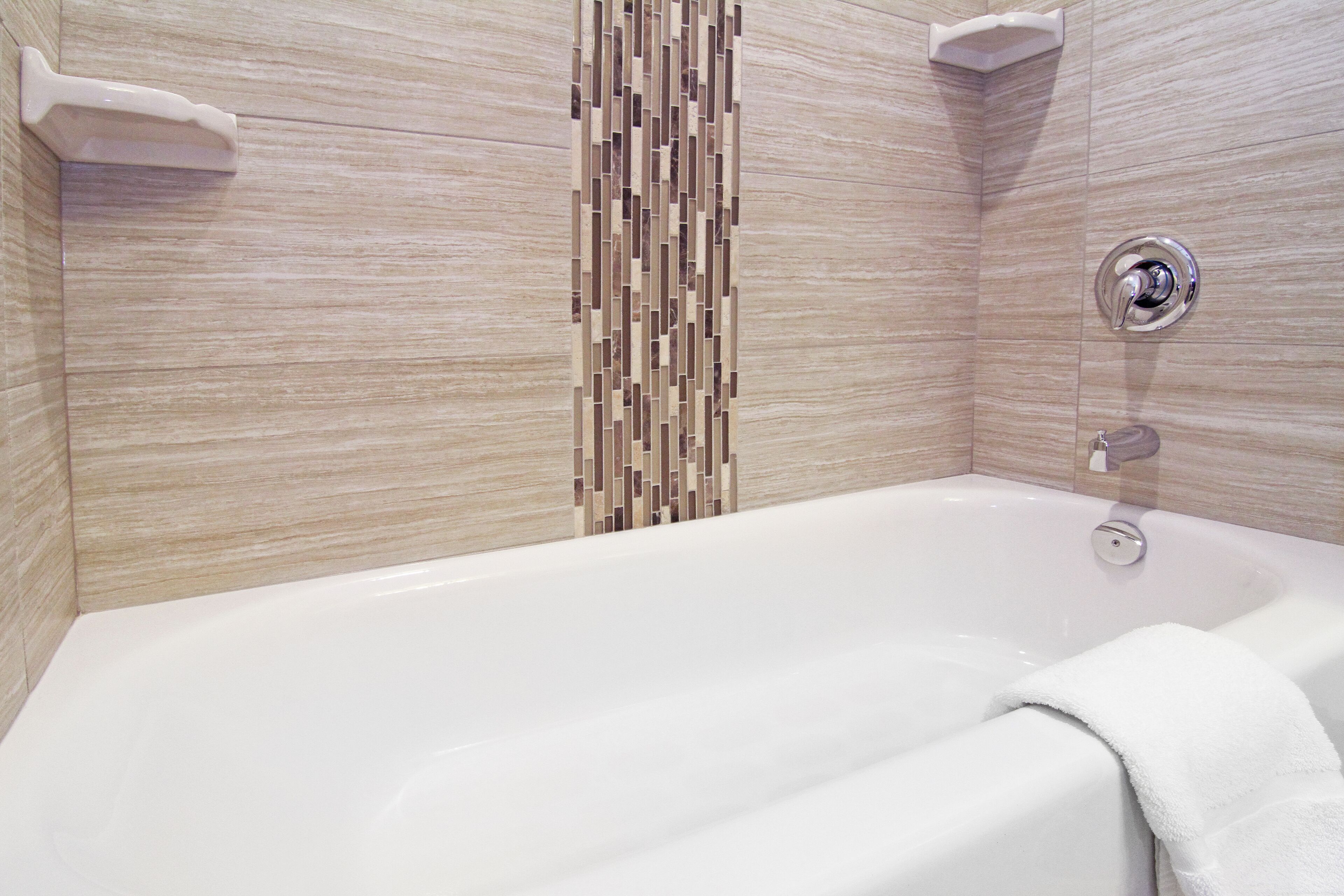 A modern bathroom with a large bathtub, a vertical mosaic wall, and a shower area.